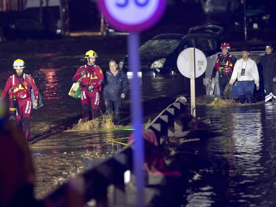 Rettungskräfte begleiten Menschen durch überflutete Strasse.