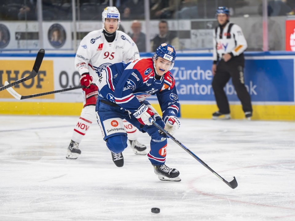 Eishockeyspieler im blauen Trikot mit Schläger bei Puck-Kontrolle.