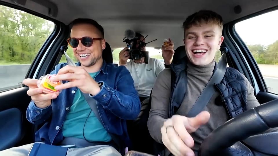 Drei Männer sitzen in einem Auto und lachen. 