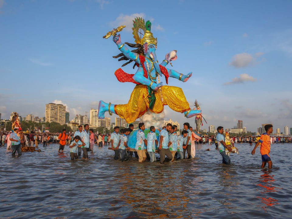 Menschen tragen eine Statue während eines religiösen Festivals im Wasser.