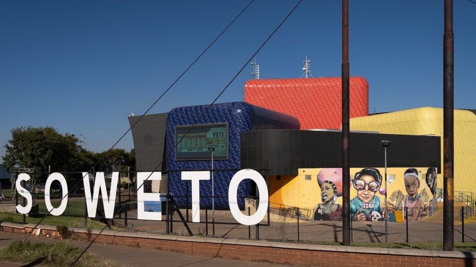 Das Soweto-Theater von aussen. Vorne dran ein weisser "Soweto"-Schriftzug. Dahinter das bunte Gebäude.