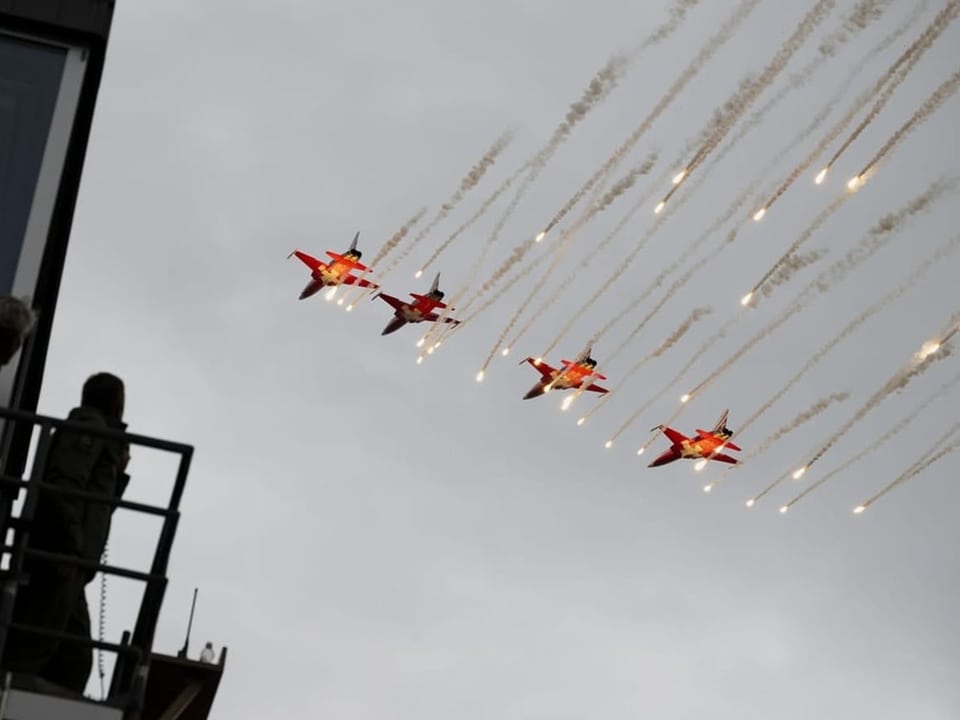 Vier jets fliegen am bewölkten Himmel und werden von Feuerwerk begleitet. 