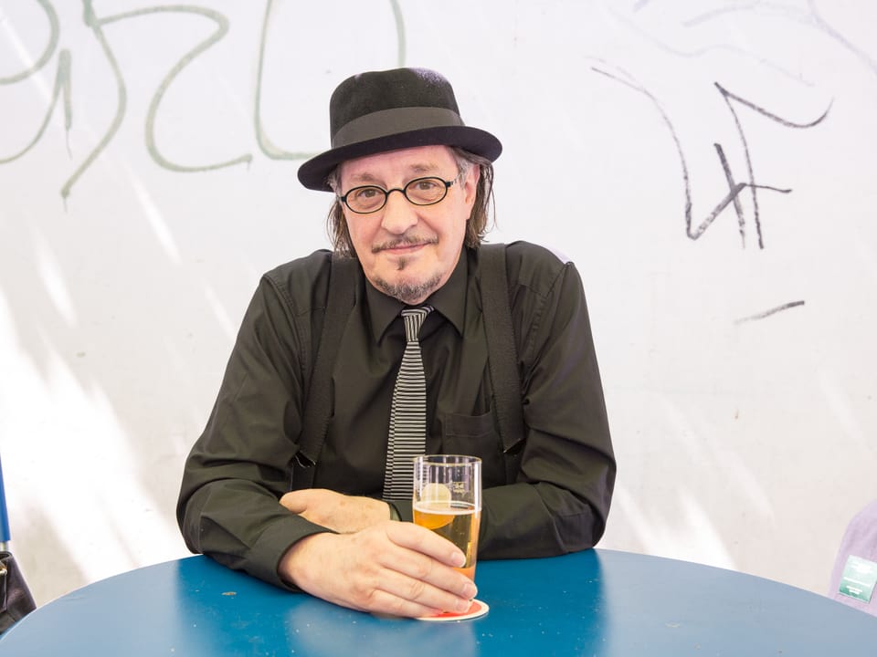 Heinz D. Heisl sitzt an einem blauen Tisch mit einem Bier.