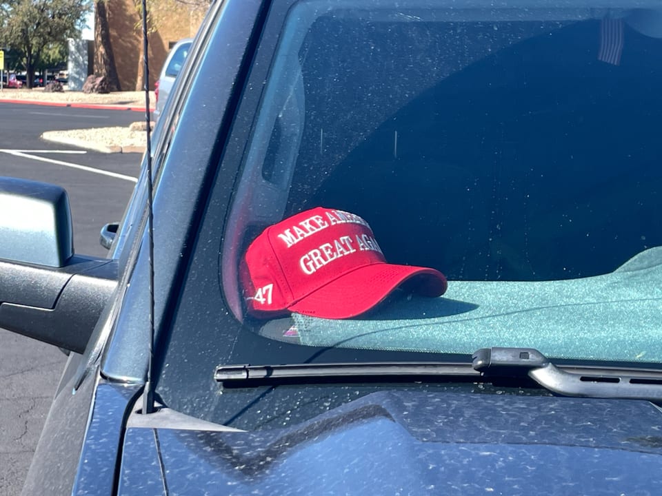 Rote Kappe mit Aufschrift 'Make America Great Again' auf Armaturenbrett eines Autos.