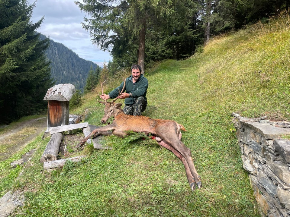 Jäger posiert mit erlegtem Hirsch auf einer Wiese im Wald.