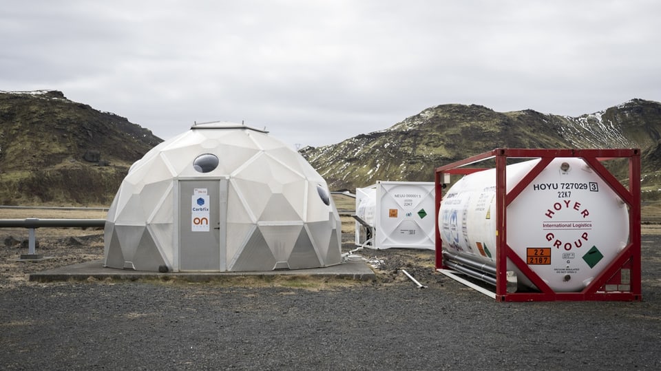 Ein zeltförmiger Bau neben zwei Container in einer kargen Landschaft in Island