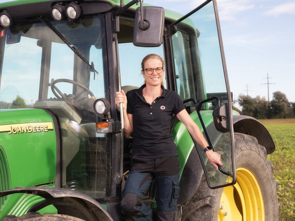 Frau steht lächelnd neben grünem Traktor.