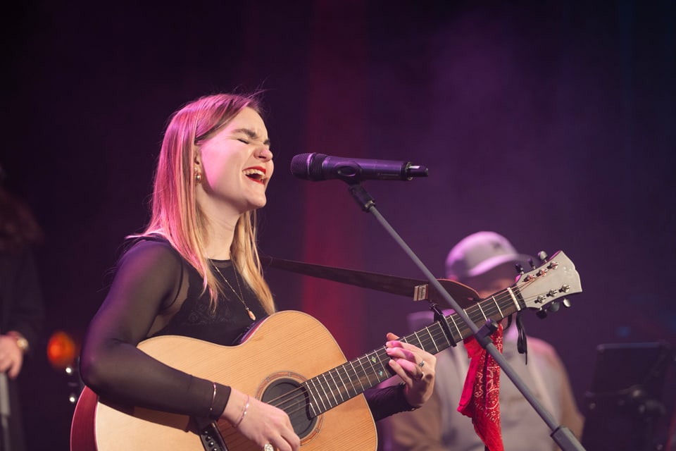 Frau singt und spielt Gitarre auf der Bühne.