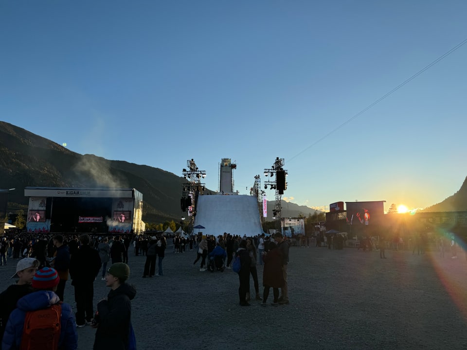 Menschenmenge bei Outdoor-Veranstaltung mit Rampe und Bühnen bei Sonnenuntergang.