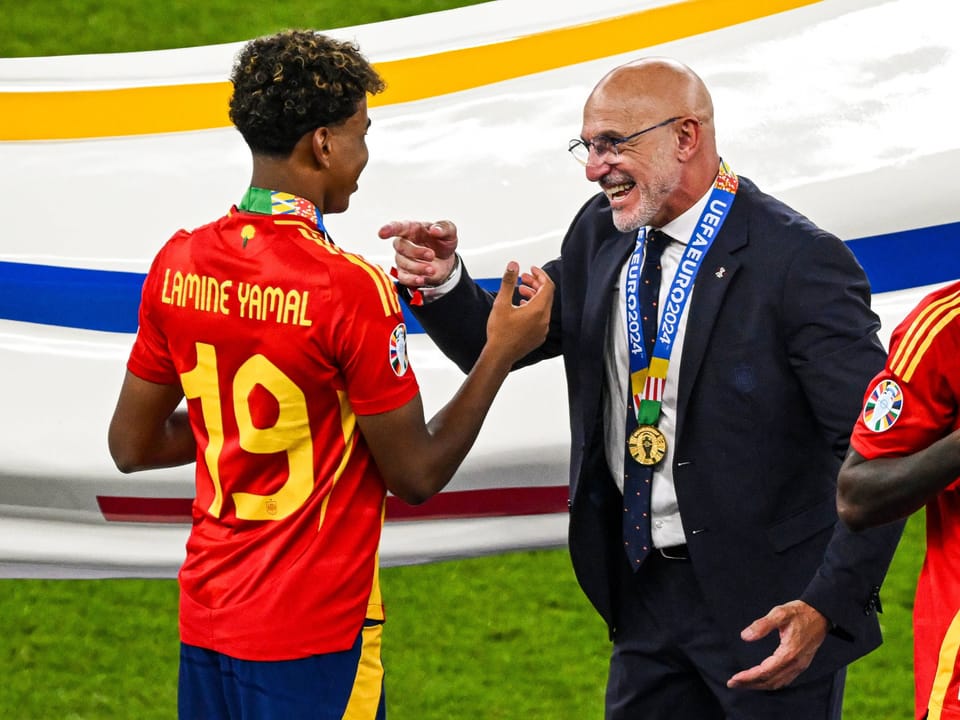 Junger spanischer Fussballspieler mit Medaille spricht mit älterem Trainer.