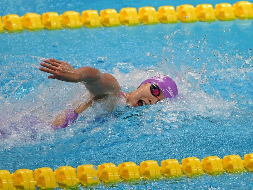 Schwimmerin im Wettkampf, Freistil, violetter Badeanzug.