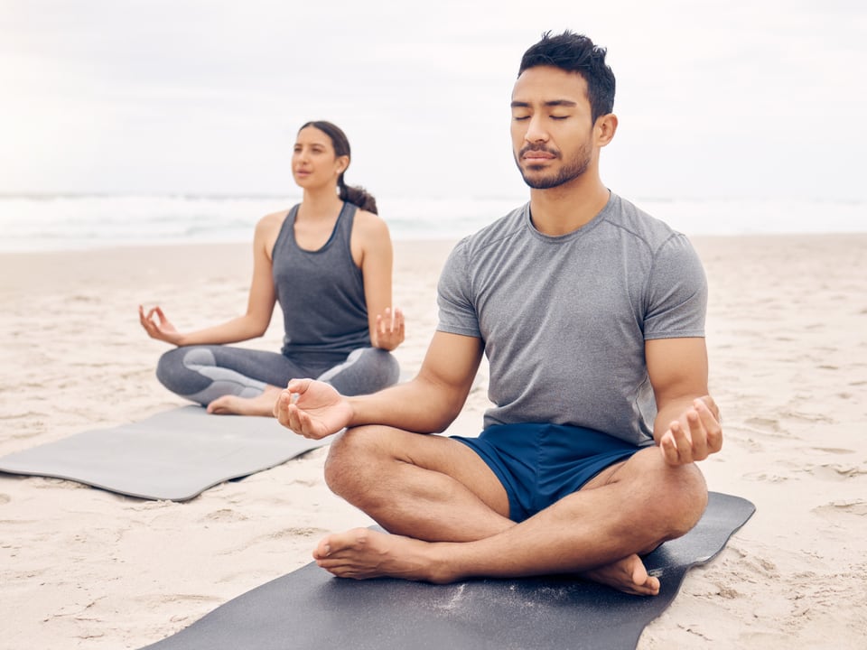 Zwei Personen praktizieren Yoga an einem Strand.