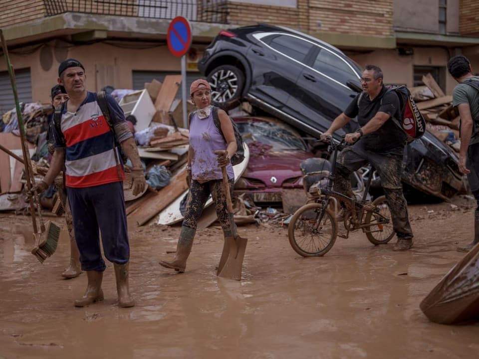 Menschen waten durch schlammiges Hochwasser mit Autotrümmern.