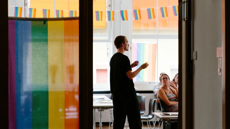 Ein Mann steht in einem Workshop-Raum voller Regenbogenflaggen.