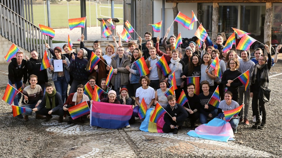 Eine Gruppe junger Menschen mit Regenbogenfahnen auf einem Kopfsteinpflasterplatz