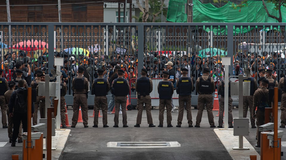 Eine Reihe von Polizisten steht einer Menge von Menschen hinter einer Gitterabsperrung gegenüber