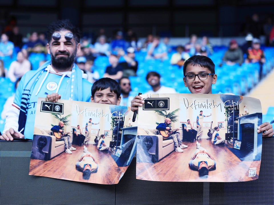 Zwei junge Fans mit Postern im Stadion mit der Aufschrift  «Definitely City» und der Band Oasis im Bild