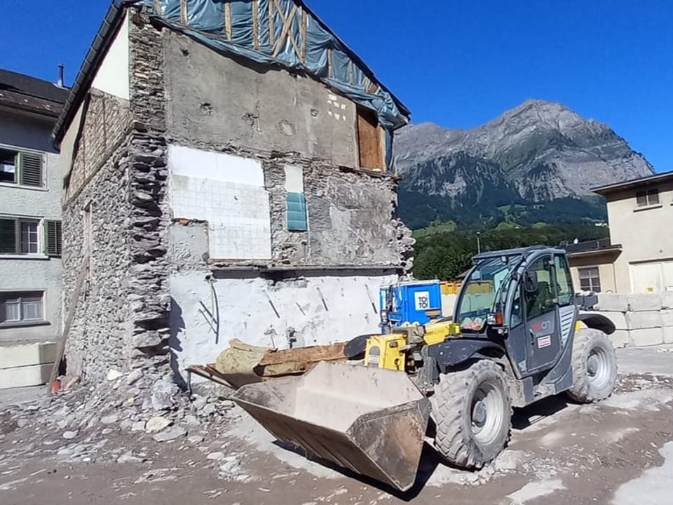 Ein Bagger vor einem Haus, das abgebrochen wird.