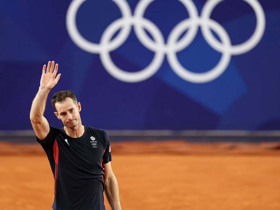 Tennisspieler winkt vor olympischen Ringen.