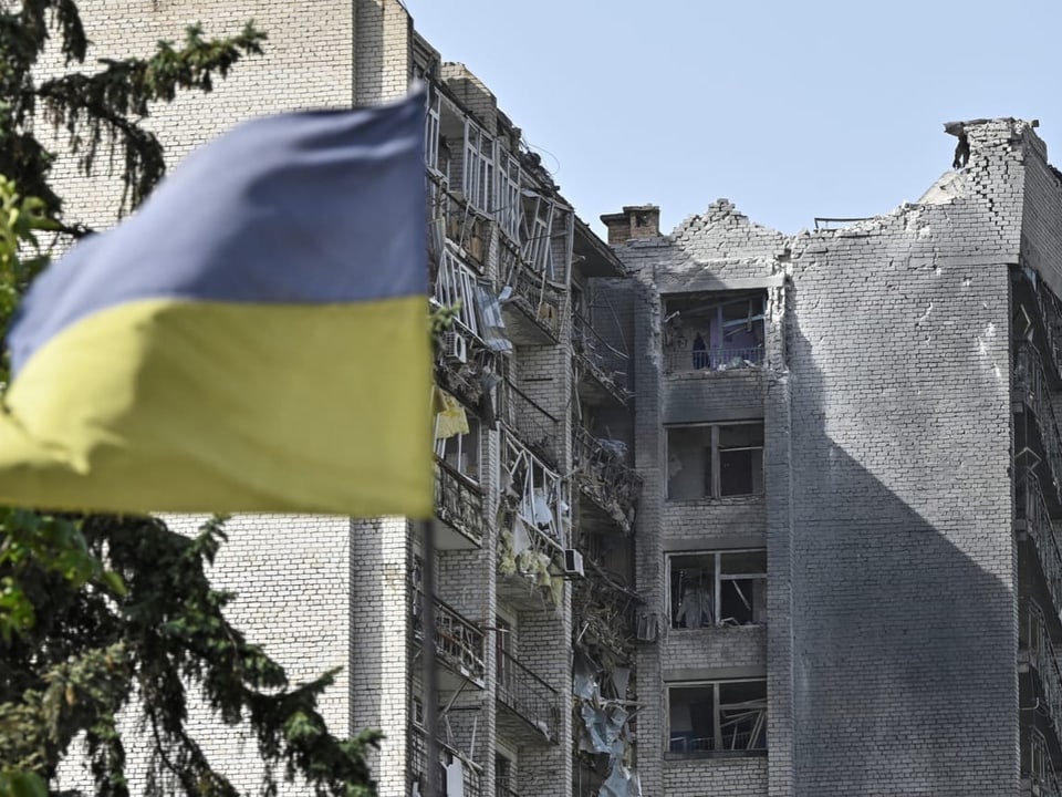 Zerstörtes Gebäude mit ukrainischer Flagge im Vordergrund.