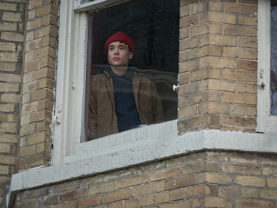 Person mit roter Mütze schaut aus einem Fenster eines Backsteingebäudes.