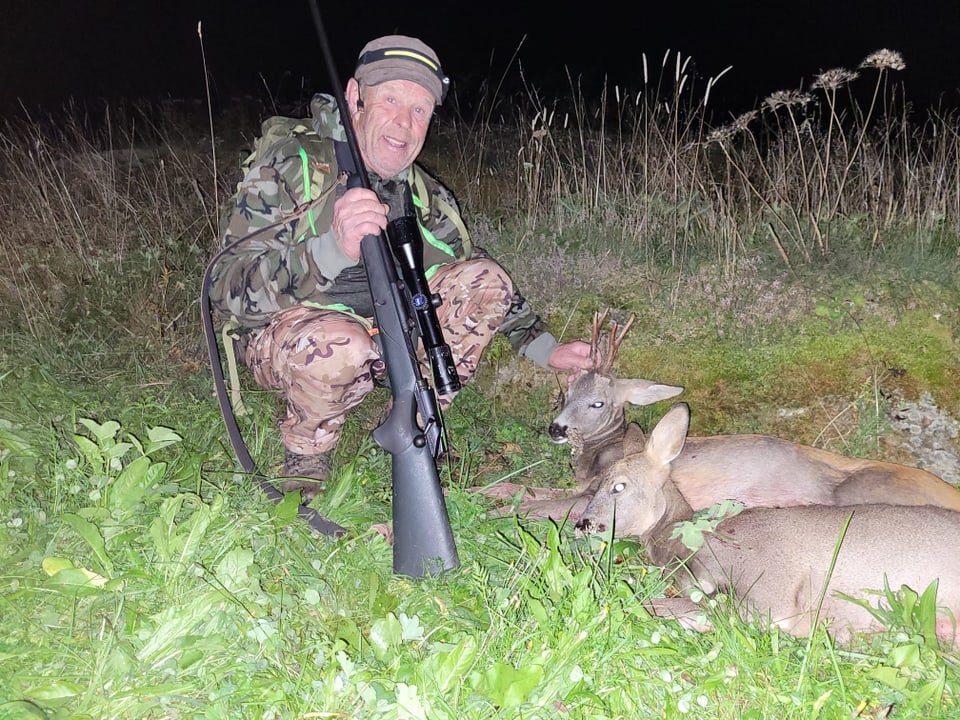 Jäger in Tarnkleidung mit erlegten Rehen auf einer Wiese.