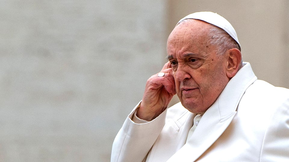 Der Papst in weisser Robe berührt sich am Kopf.