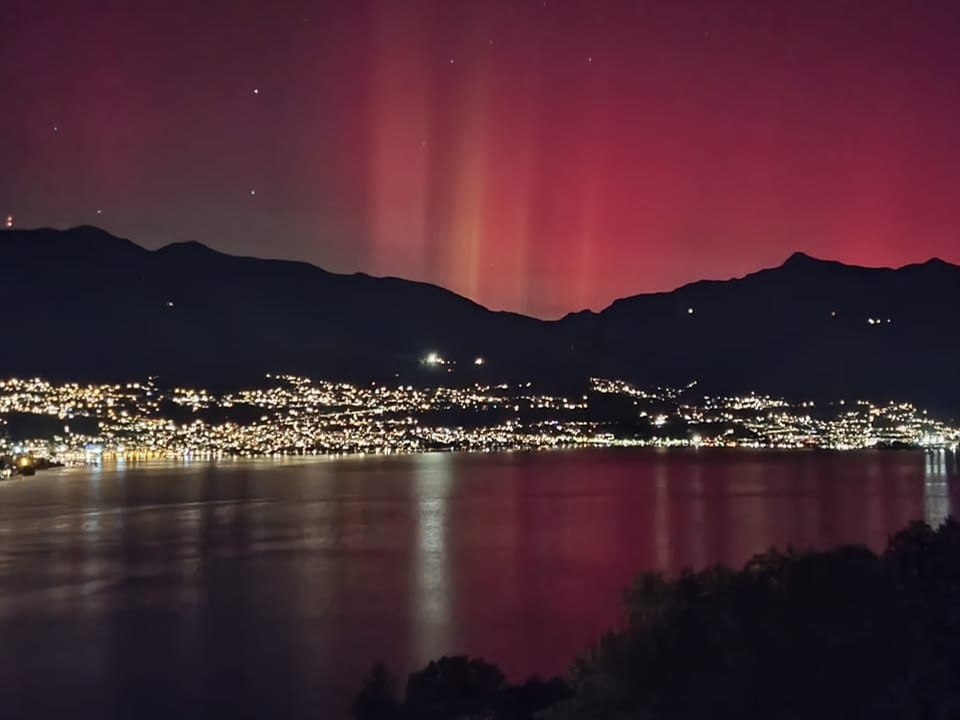 Rote Nordlichter über Bergen und See bei Nacht.