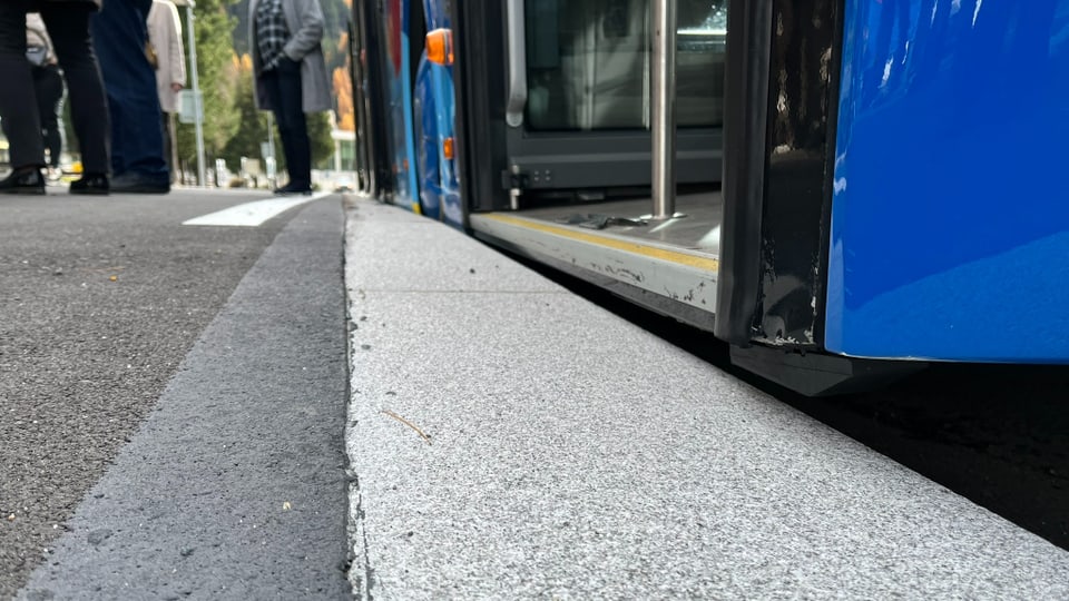 Nahaufnahme eines blauen Busses an der Bordsteinkante mit Menschen im Hintergrund.