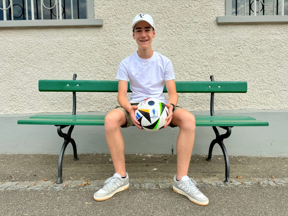 Junge sitzt auf Bank mit Fussball in der Hand