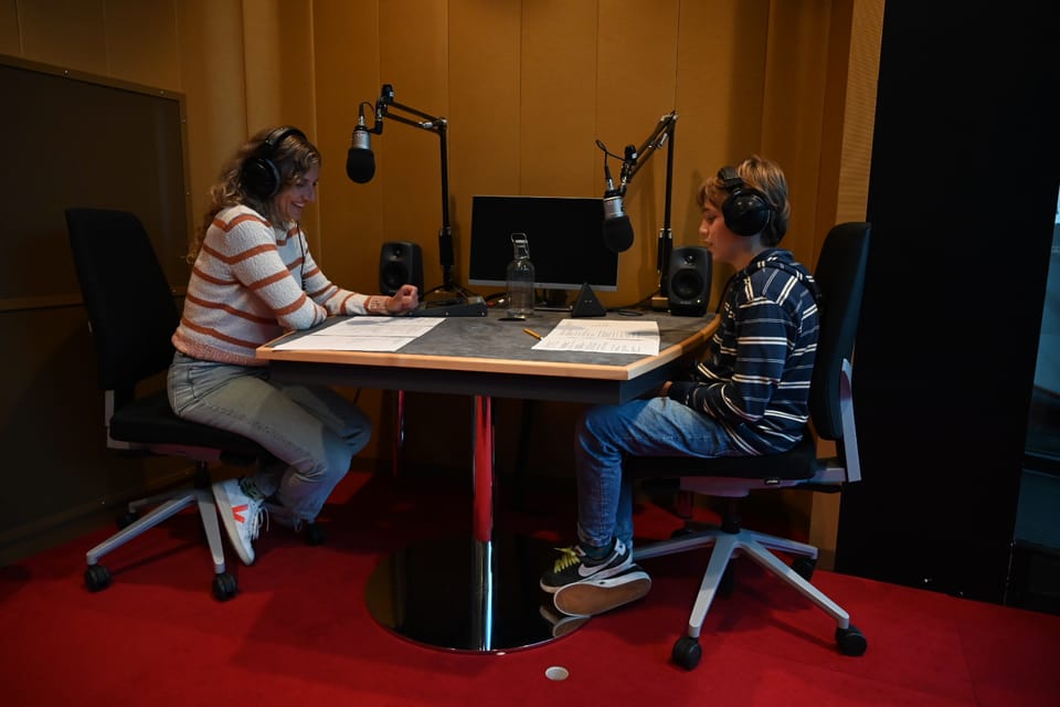 Zwei Personen in einem Tonstudio am Tisch, tragen Kopfhörer.