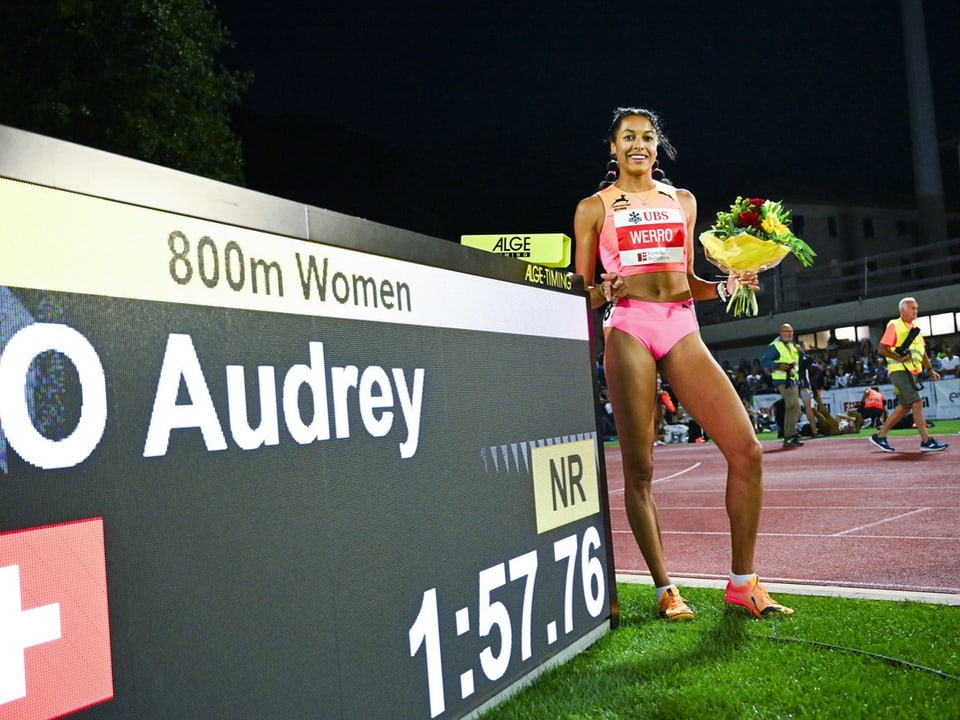 Läuferin bei 800m Frauen-Rennen hält Blumenstrauss neben Anzeigetafel mit Zeit.