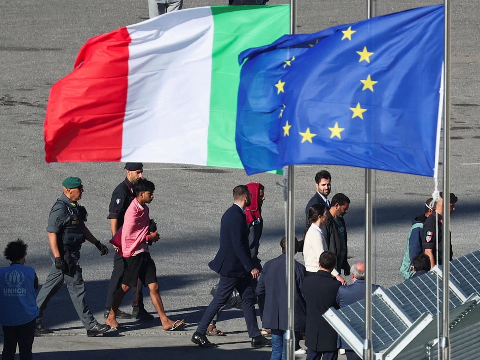 Menschen gehen unter italienischer und EU-Flagge.