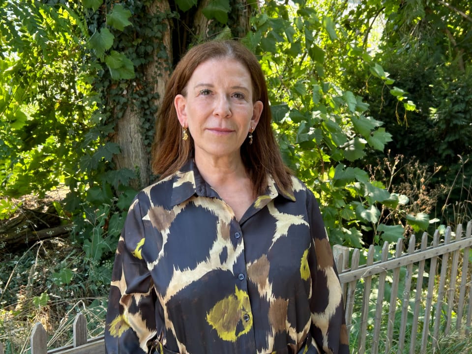Frau steht vor einem baumbedeckten Hintergrund neben einem Zaun.