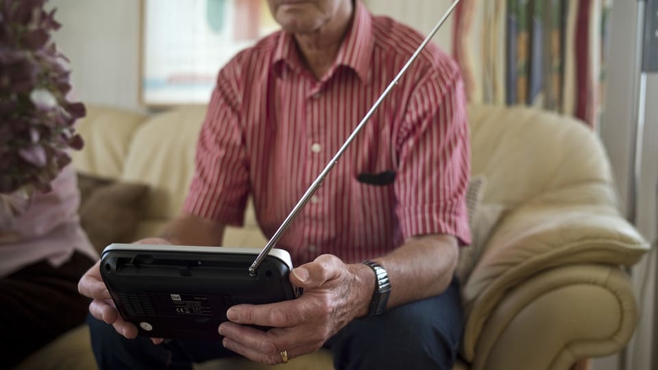 Älterer Mann mit einem Radiogerät mi Antenne in der Hand.
