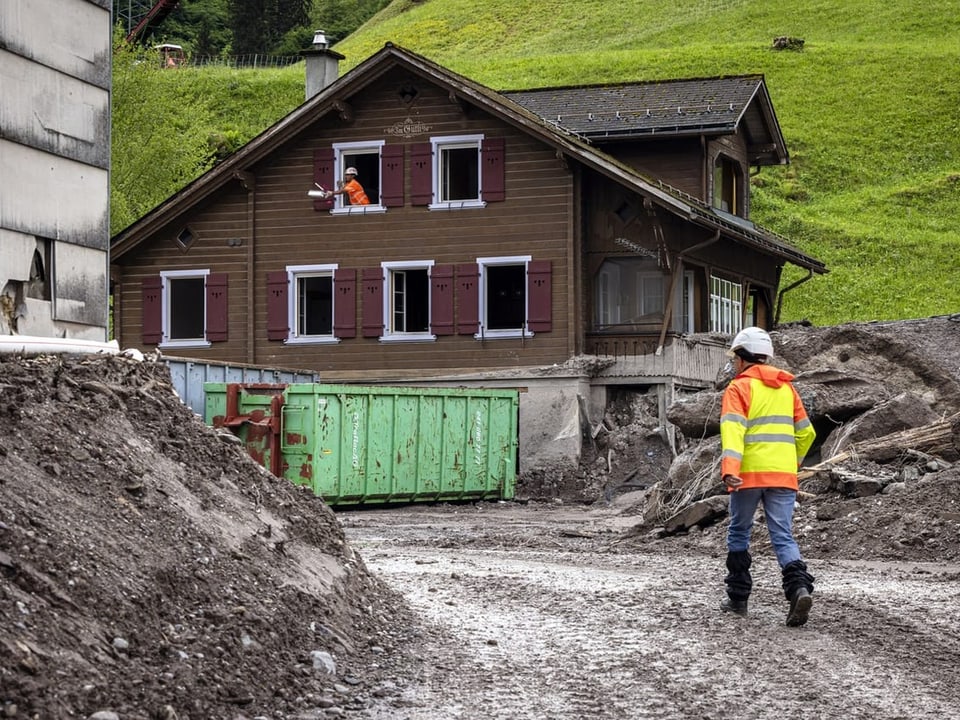 Bauarbeiter vor einem Holzhaus und Erdarbeiten.