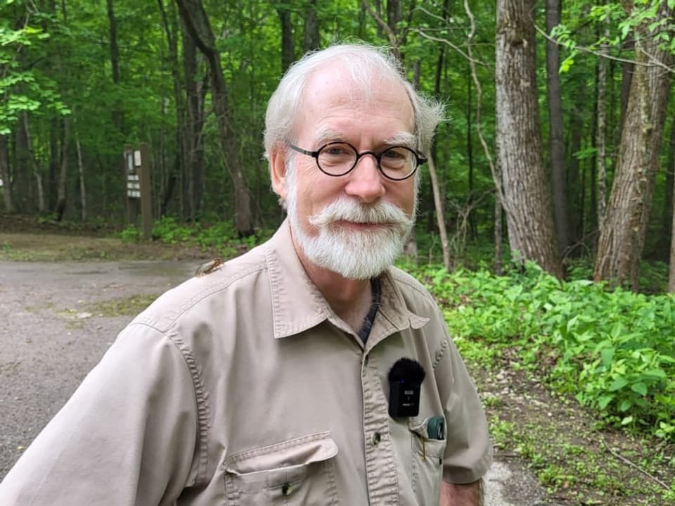 Älterer Mann mit Brille und Bart in Waldumgebung.