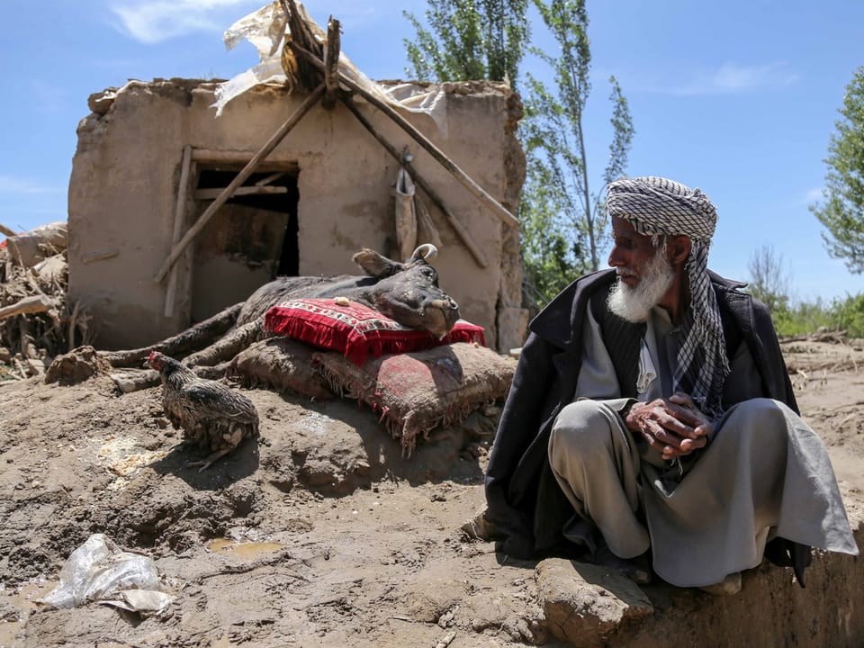 Ein Mann mit afghanischer Kleidung sitzt vor seinem zerstörten, einfachen Haus.