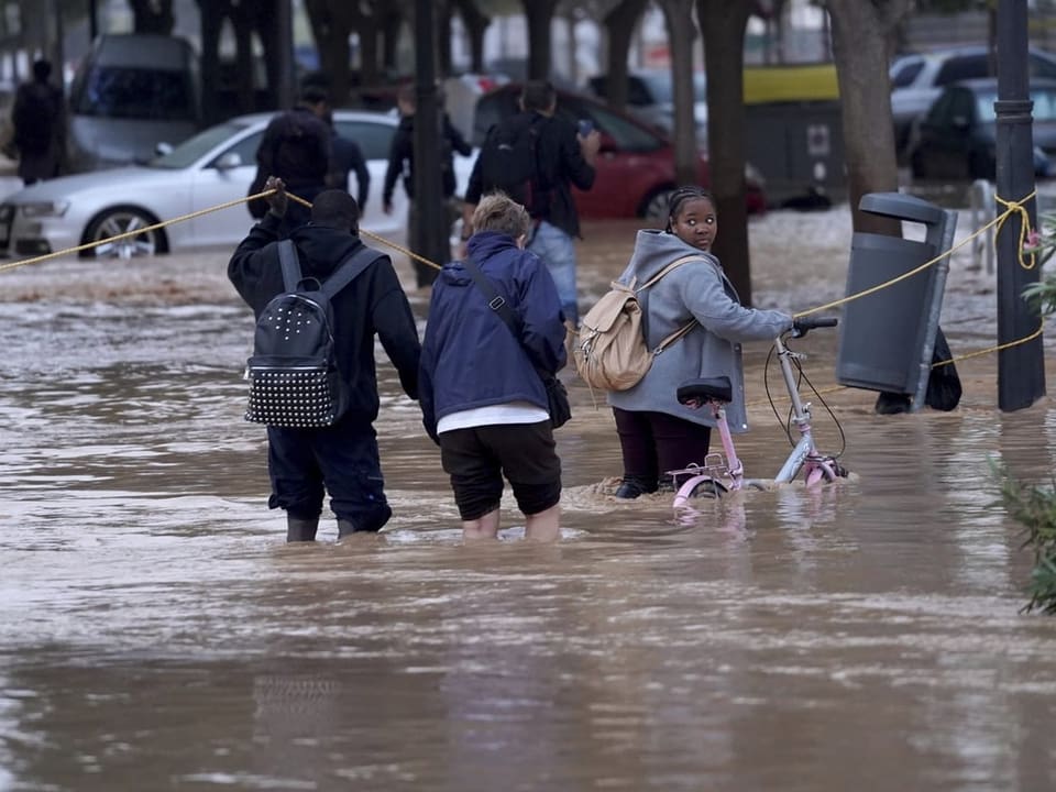 Menschen waten durch überflutete Strasse mit Autos im Hintergrund.