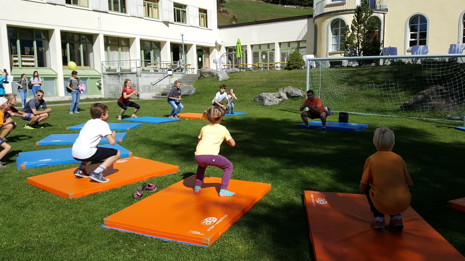 En in mez rintg stan uffants e creschids sin mattas da gimnastica blauas ed orandschas e fan gimnastica sin instrucziun da Nevin Galmarini che stà en la mitad dal mez rintg.