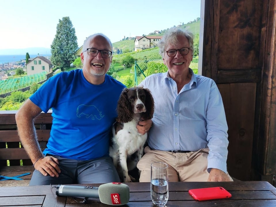 Marcel Hähni, Hund Daisy und Weinpatron Patrick Fonjallaz sitzen nebeneinander auf einer Bank im Garten.