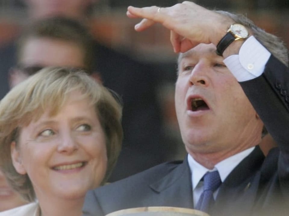 Merkel lacht, während Bush Faxen macht
