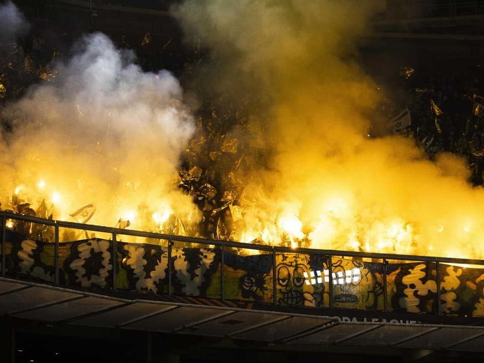 Fussballfans zünden gelbe Rauchbomben im Stadion.