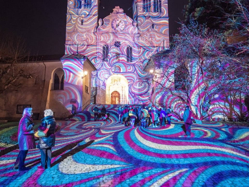 Zwei Frauen stehen vor einer Kirche, die mit bunten, spiraligen Mustern beleuchtet ist.