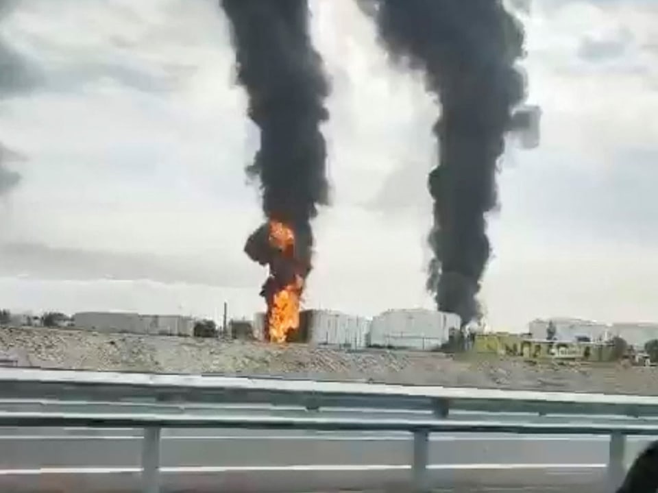 Schwarzer Rauch und Flammen neben einer Strasse.