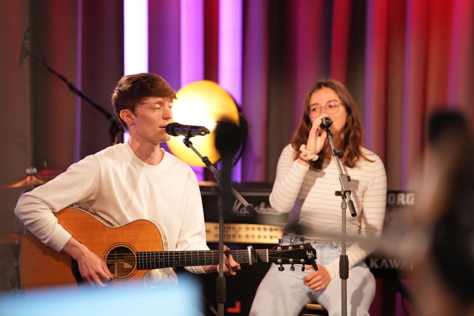 Zwei Musiker singen und spielen Gitarre in einem Studio.