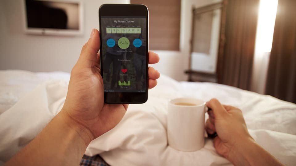 Mann schaut Smartphone mit Vitaldaten im Bett an.