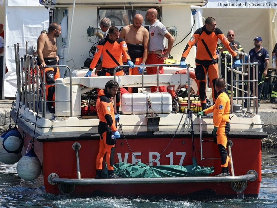 Rettungssanitäter in orangefarbenen Anzügen auf einem Rettungsboot im Hafen.