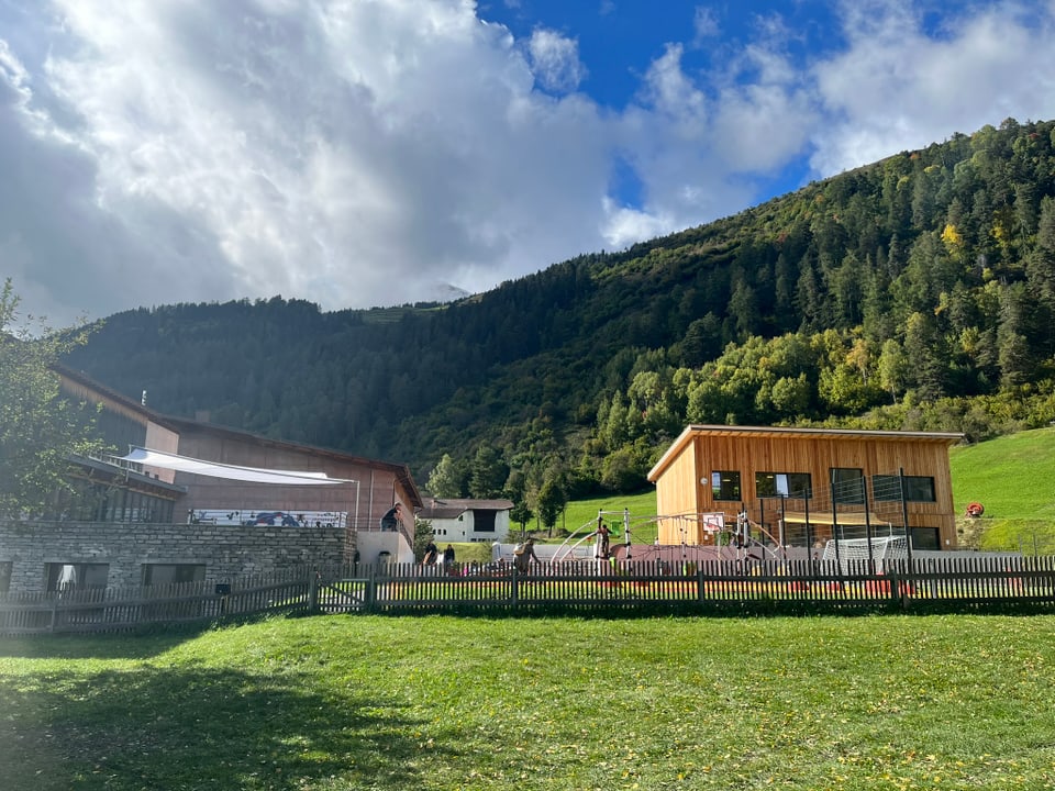 Gebäude mit Spielplatz und Bergen im Hintergrund.