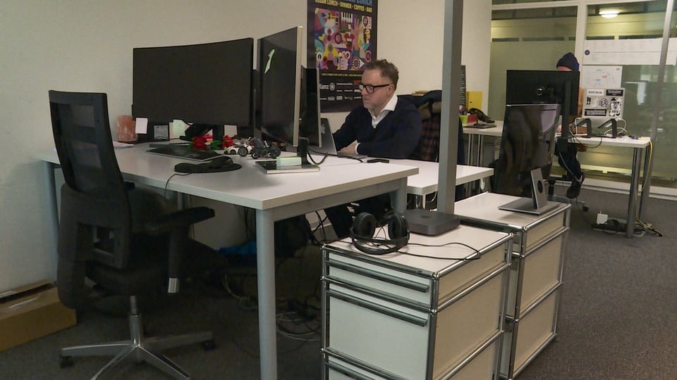 Michael sitzt an seinem Arbeitsplatz in einem grösseren Büro. 